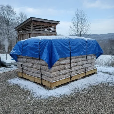 Outdoor wood pellet storage for winter, covered with a tarp and elevated on a pallet.